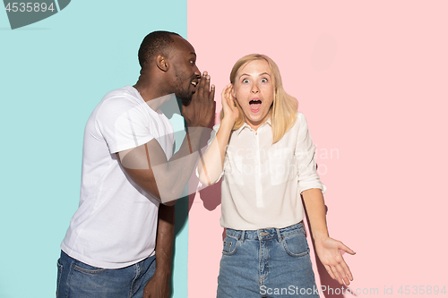 Image of The young couple whispering a secret behind her hand over studio background