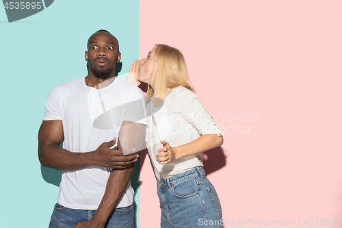 Image of The young couple whispering a secret behind her hand over studio background