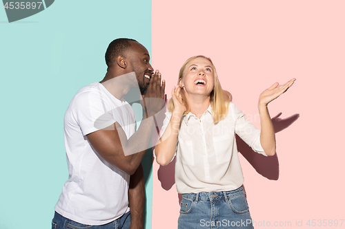 Image of The young couple whispering a secret behind her hand over studio background