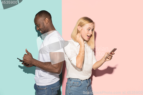 Image of Mixed raced couple of students taking mobile phones. Caucasian girl and her African boyfriend posing at studio .