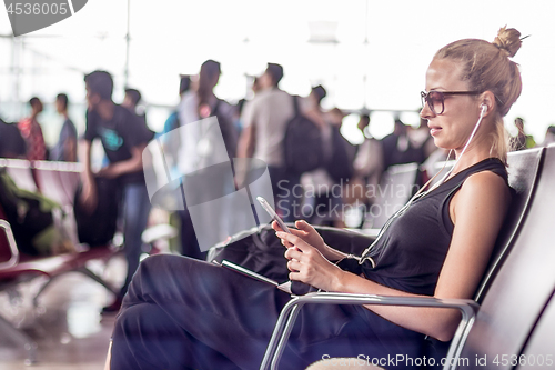 Image of Female traveler using her cell phone while waiting to board a plane at departure gates at asian airport terminal.