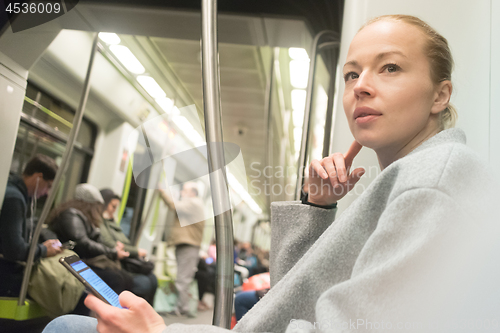 Image of Beautiful blonde woman using smart phone while traveling by metro public transport.