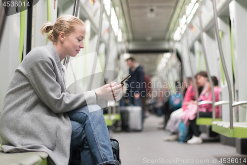 Image of Beautiful blonde woman wearing winter coat reading on the phone while traveling by metro public transport.