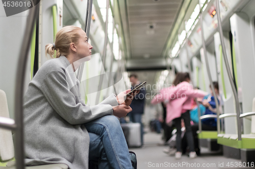 Image of Beautiful blonde woman using smart phone while traveling by metro public transport.