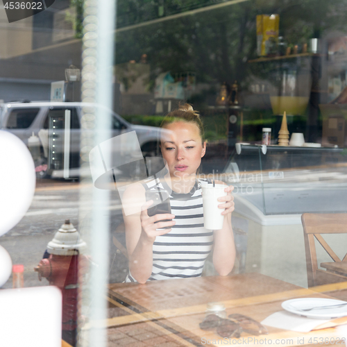 Image of Thoughtful woman reading news on mobile phone during rest in coffee shop.