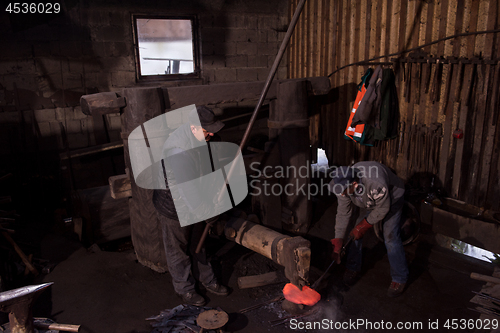 Image of blacksmith workers using mechanical hammer at workshop