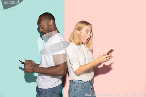 Image of Mixed raced couple of students taking mobile phones. Caucasian girl and her African boyfriend posing at studio .