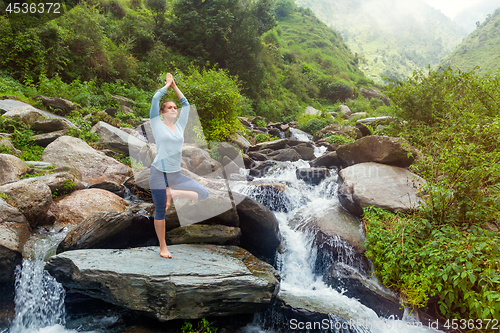 Image of Woman in yoga asana Vrikshasana tree pose at waterfall outdoors