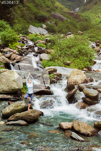 Image of Woman in yoga asana Vrikshasana tree pose at waterfall outdoors