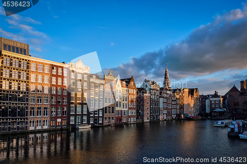 Image of Hhouses and tourist boats on Amsterdam canal pier Damrak on suns