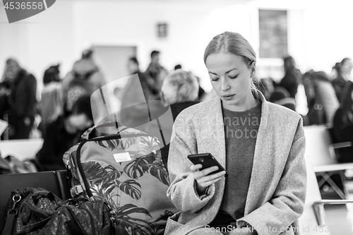 Image of Female traveler reading on her cell phone while waiting to board a plane at departure gates at airport terminal.