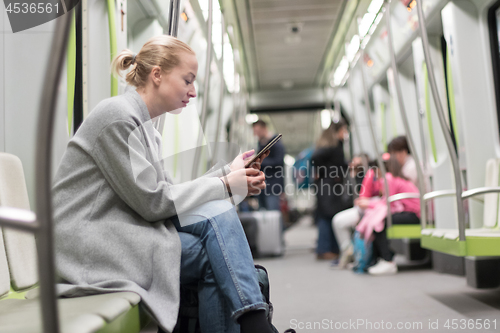 Image of Beautiful blonde woman using smart phone while traveling by metro public transport.