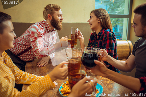 Image of people, leisure, friendship and communication concept - happy friends drinking beer, talking and clinking glasses at bar or pub