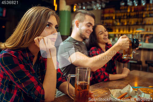 Image of people, leisure, friendship and communication concept - happy friends drinking beer, talking and clinking glasses at bar or pub