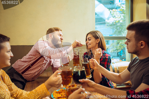 Image of people, leisure, friendship and communication concept - happy friends drinking beer, talking and clinking glasses at bar or pub