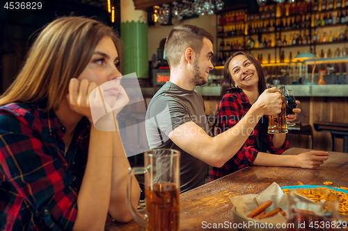 Image of people, leisure, friendship and communication concept - happy friends drinking beer, talking and clinking glasses at bar or pub