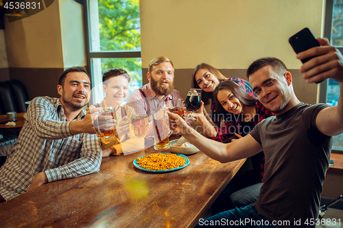 Image of people, leisure, friendship and communication concept - happy friends drinking beer, talking and clinking glasses at bar or pub