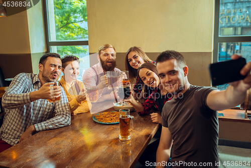 Image of people, leisure, friendship and communication concept - happy friends drinking beer, talking and clinking glasses at bar or pub