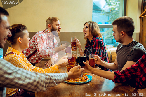 Image of people, leisure, friendship and communication concept - happy friends drinking beer, talking and clinking glasses at bar or pub