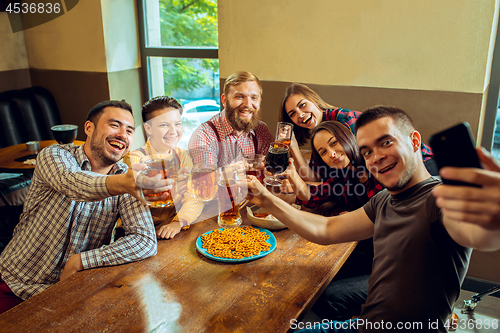 Image of people, leisure, friendship and communication concept - happy friends drinking beer, talking and clinking glasses at bar or pub