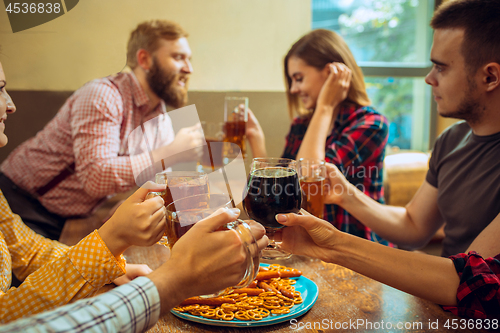 Image of people, leisure, friendship and communication concept - happy friends drinking beer, talking and clinking glasses at bar or pub