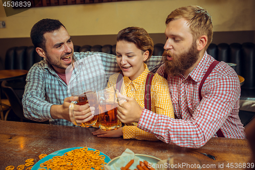 Image of people, leisure, friendship and communication concept - happy friends drinking beer, talking and clinking glasses at bar or pub