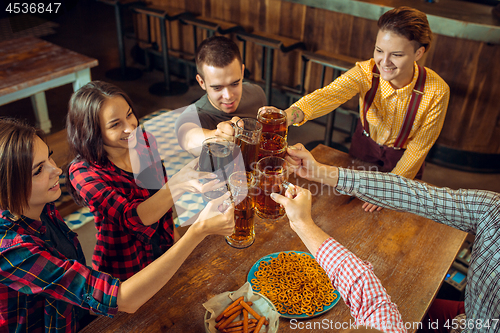 Image of people, leisure, friendship and communication concept - happy friends drinking beer, talking and clinking glasses at bar or pub