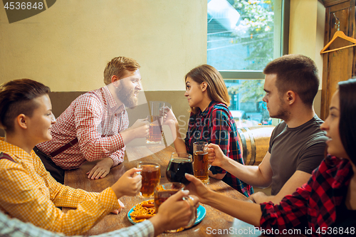 Image of people, leisure, friendship and communication concept - happy friends drinking beer, talking and clinking glasses at bar or pub