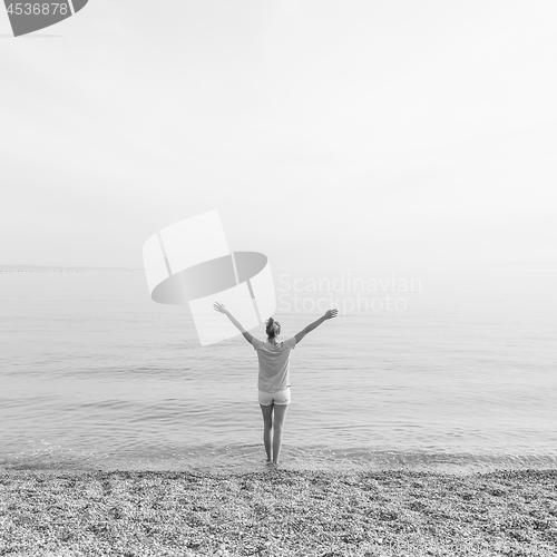 Image of Happy Carefree Woman Enjoying Sunset Walk on White Pabbled Beach. Black and white photo.