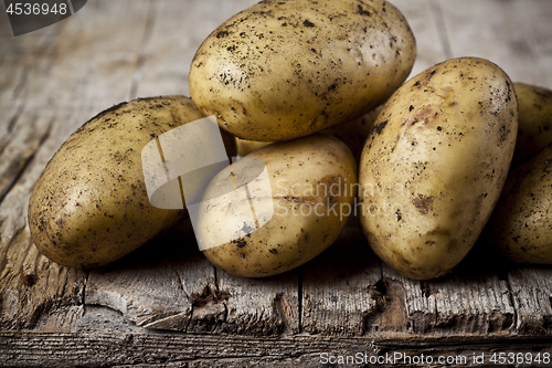 Image of Newly harvested dirty potatoes heap on rustic wooden background.