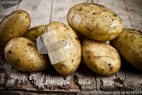 Image of Newly harvested dirty potatoes heap on rustic wooden background.