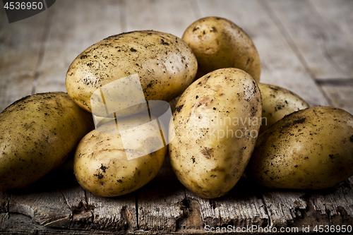 Image of Newly harvested dirty potatoes heap on rustic wooden background.