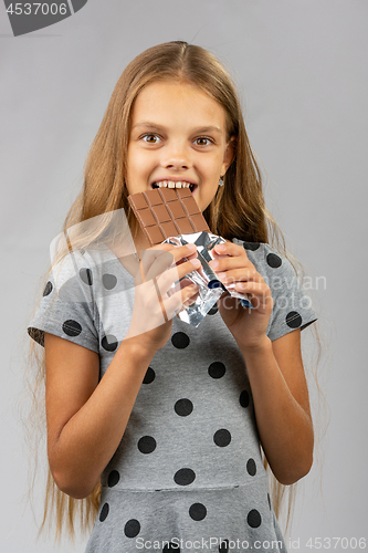 Image of Ten-year girl bites chocolate and happily looks into the frame