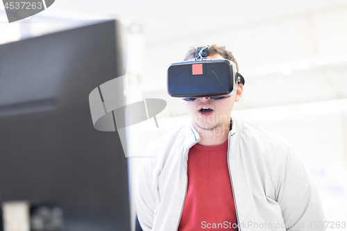 Image of Young man wearing virtual reality headset and gesturing while sitting at his desk in creative office