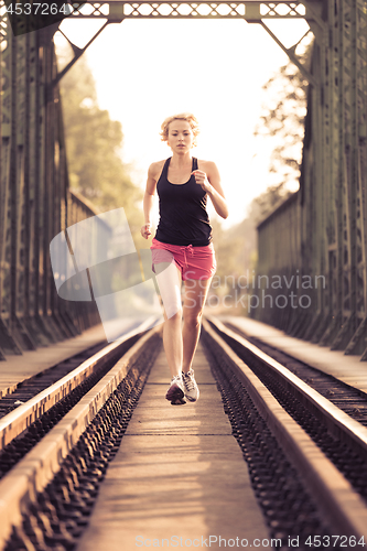 Image of Active sporty woman running on railroad tracks.