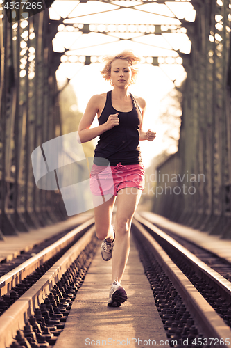 Image of Active sporty woman running on railroad tracks.