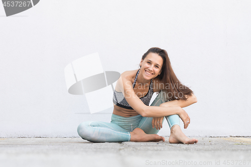 Image of Fit sporty active girl in fashion sportswear sitting on the floor in front of gray wall.