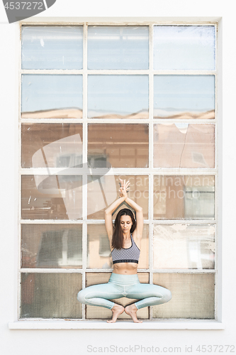 Image of Fit sporty active girl in fashion sportswear doing yoga fitness exercise in front of gray wall, outdoor sports, urban style