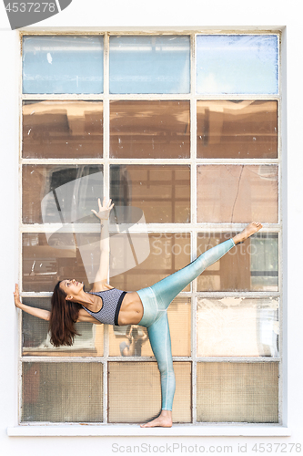 Image of Fit sporty active girl in fashion sportswear doing yoga fitness exercise in front of gray wall, outdoor sports, urban style