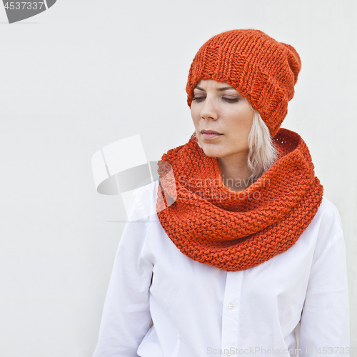 Image of Pretty young woman in warm orange knitted hat and snood.