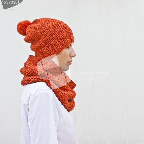 Image of Pretty young woman in warm orange knitted hat and snood. 