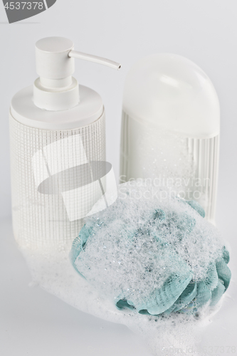 Image of Liquid soap, lotion, green sponge and foam on light background.