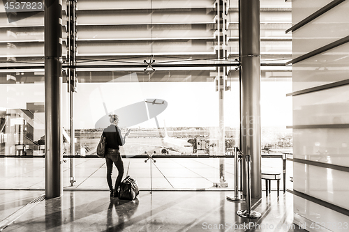 Image of Young woman waiting at airport, looking through the gate window.