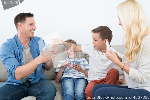 Image of Happy young family playing card game at home.