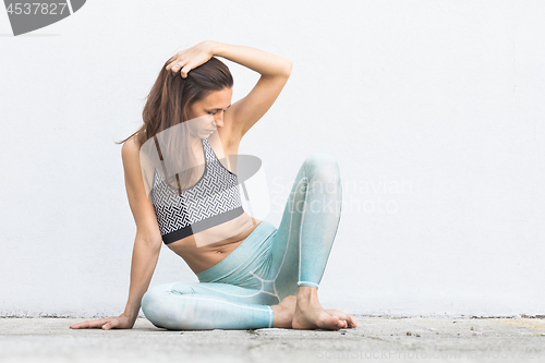 Image of Fit sporty active girl in fashion sportswear sitting on the floor in front of gray wall.