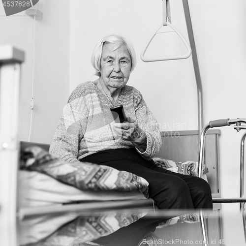 Image of Elderly 96 years old woman operating TV or DVD with remote control in black and white.