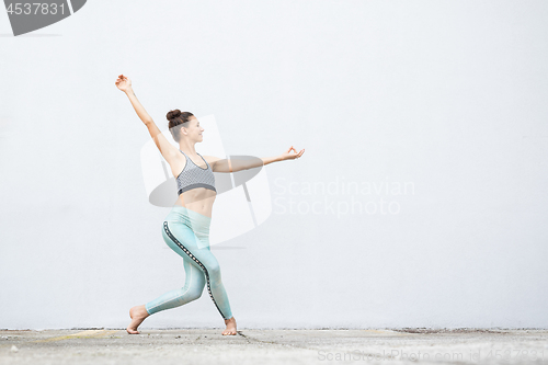 Image of Fit sporty active girl in fashion sportswear doing yoga fitness exercise in front of gray wall, outdoor sports, urban style