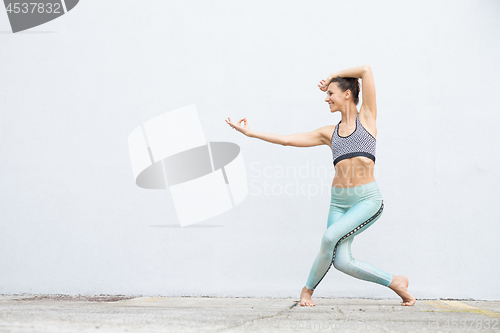 Image of Fit sporty active girl in fashion sportswear doing yoga fitness exercise in front of gray wall, outdoor sports, urban style