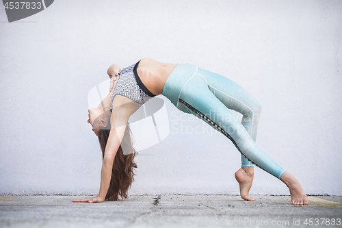 Image of Fit sporty active girl in fashion sportswear doing yoga fitness exercise in front of gray wall, outdoor sports, urban style