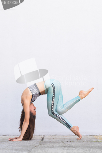 Image of Fit sporty active girl in fashion sportswear doing yoga fitness exercise in front of gray wall, outdoor sports, urban style